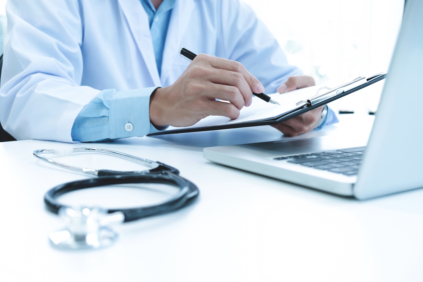 Médico trabalhando com notebook e escrevendo em papel